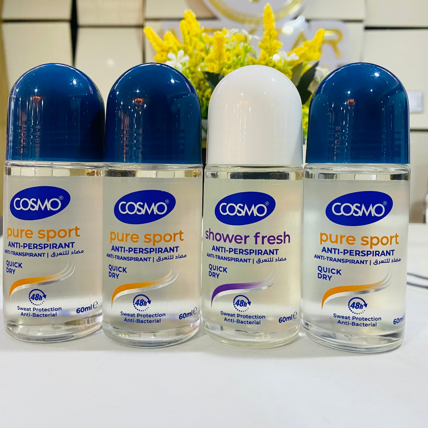 Four bottles of Cosmo deodorant on a white surface with a blurred background