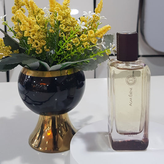 Perfume bottle with a decorative vase and flowers on a white surface.