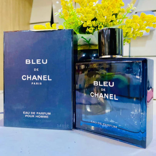 Bleu de Chanel perfume bottle and packaging on a white surface with yellow flowers in the background.
