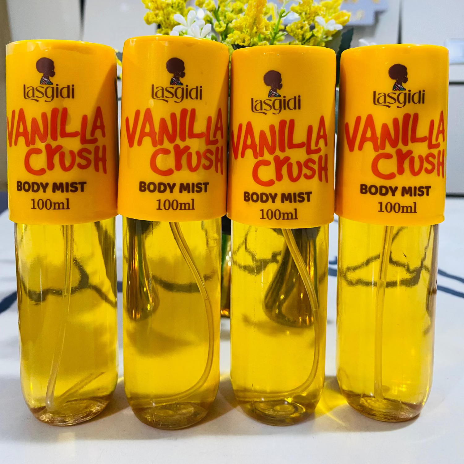 Four bottles of Lasgidi Vanilla Crush body mist on a white surface with a blurred background.