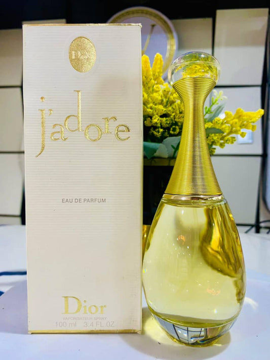 Dior j'adore perfume bottle and packaging on a table with flowers in the background